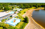 Luftaufnahme vom Camping de Schatberg in Limburg, mit Pool, Wasserrutschen und Sandstrand am See.