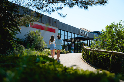 Two people walk towards the entrance of Camping de Schatberg holiday park in Limburg, Netherlands, in summer.