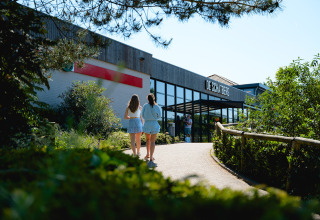 Two people walk towards the entrance of Camping de Schatberg holiday park in Limburg, Netherlands, in summer.