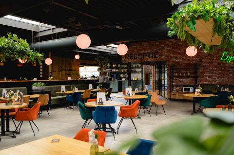 Modern restaurant interior at Camping de Schatberg in Limburg, Netherlands, with colorful chairs and plants.