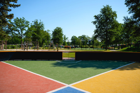 A colorful sports field and playground at Camping de Schatberg, Limburg, Netherlands, surrounded by green trees.