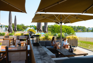 Outdoor seating at Camping de Schatberg, Limburg, Netherlands, overlooking a lake and green scenery.