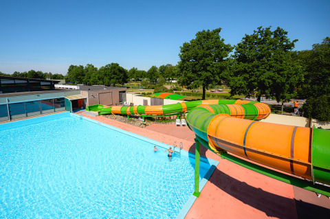 Outdoor pool and colorful water slides at Camping de Schatberg holiday park in Limburg, Netherlands, on a sunny day.