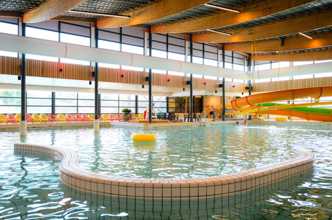 Indoor pool with a waterslide and colorful lounge chairs at Camping de Schatberg in Limburg, Netherlands.