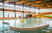 Indendørs swimmingpool med vandrutsjebane og farverige stole ved Camping de Schatberg, Limburg, Holland.