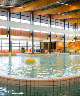 Piscina cubierta con tobogán de agua y sillas coloridas en Camping de Schatberg, Limburg, Países Bajos.