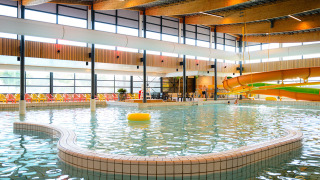 Piscina cubierta con tobogán de agua y sillas coloridas en Camping de Schatberg, Limburg, Países Bajos.