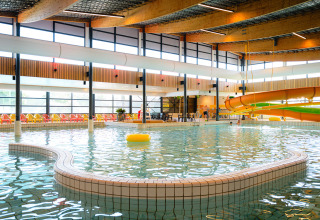 Indoor pool with a waterslide and colorful lounge chairs at Camping de Schatberg in Limburg, Netherlands.