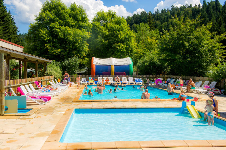 Outdoor swimming pool at Camping de Vaubarlet in Auvergne-Rhône-Alpes, France, with families enjoying the sun.