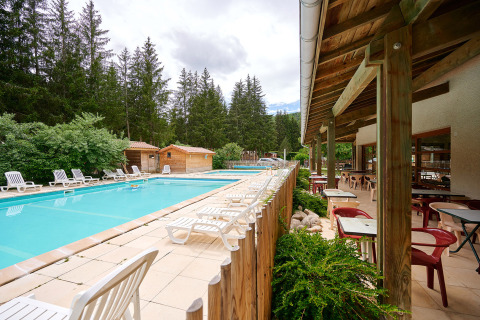 Outdoor swimming pool with loungers and terrace seating area at Camping de Vaubarlet in Auvergne-Rhône-Alpes, France.