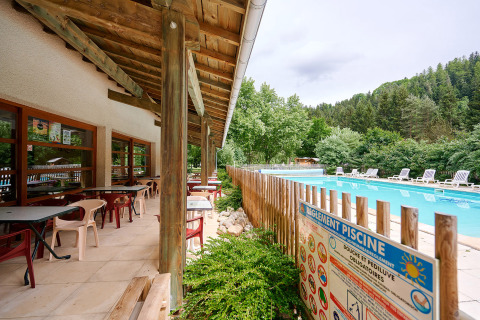 Terraza al aire libre con mesas junto a la piscina en Camping de Vaubarlet en Auvernia-Ródano-Alpes, Francia.
