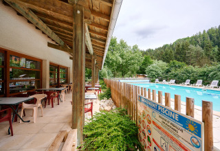 Buitenterras met tafels en stoelen bij het zwembad op Camping de Vaubarlet in Auvergne-Rhône-Alpes, Frankrijk.