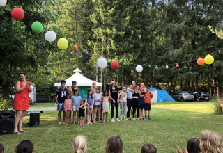 Bambini e adulti festeggiano all’aperto sotto lanterne colorate al Camping de Vaubarlet in Francia.
