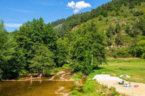 Persone che si rilassano su una spiaggia fluviale tra colline verdi a Camping de Vaubarlet, Francia.