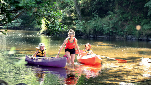 Un adulto ayuda a dos niños en kayaks sobre un río poco profundo en Camping de Vaubarlet, Auvergne-Rhône-Alpes, Francia.