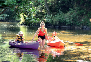 Een volwassene helpt twee kinderen in kajaks op een ondiepe rivier bij Camping de Vaubarlet, Auvergne-Rhône-Alpes.