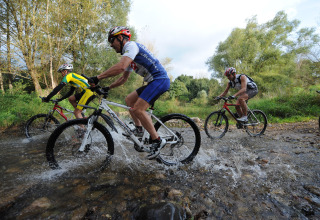 Cyclists ride mountain bikes through a rocky stream at Camping de Vaubarlet in Auvergne-Rhône-Alpes, France.
