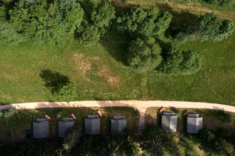 Vista aérea de cinco pequeñas cabañas junto a un sendero, rodeadas de césped y árboles en Camping de Vaubarlet.
