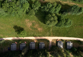 Vista aerea di cinque piccole cabine lungo un sentiero tra erba e alberi al Camping de Vaubarlet, in Francia.