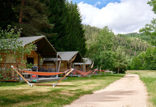 Safaritenten met hangmatten naast het pad op Camping de Vaubarlet, Auvergne-Rhône-Alpes, Frankrijk.