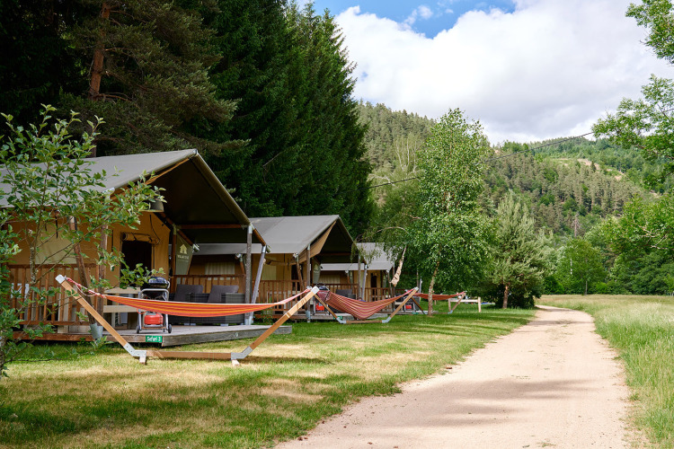Safari tents and hammocks at Camping de Vaubarlet holiday park in Auvergne-Rhône-Alpes, France, with trees.