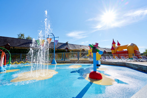 Zona de juegos acuáticos infantil con fuentes, tumbonas y castillo hinchable en Domaine du Logis, Bretaña, Francia.