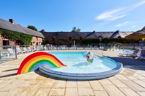 Piscina infantil con arcoíris y figuras divertidas en Camping Domaine du Logis, parque de vacaciones en Bretaña, Francia.