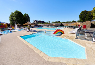 Piscina al aire libre con tumbonas y arcoíris en Camping Domaine du Logis, Bretaña, Francia, en verano.
