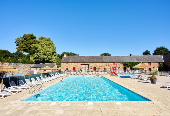 Outdoor swimming pool with sun loungers at Camping Domaine du Logis in Brittany, France, under blue sky.