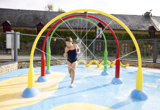 Bambino che gioca sotto archi d’acqua colorati nell’area giochi del Camping Domaine du Logis, Bretagna, Francia.