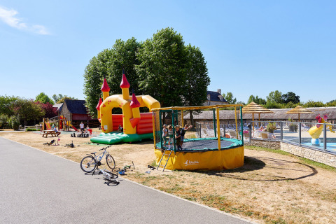 Bambini che giocano vicino a un castello gonfiabile, trampolino e piscina al Camping Domaine du Logis in Bretagna, Francia.