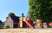 Spielplatz mit Rutsche und Bäumen am Camping Domaine du Logis in der Bretagne, Frankreich.