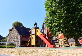 Parque infantil con tobogán y árboles en Camping Domaine du Logis, parque vacacional en Bretaña, Francia.