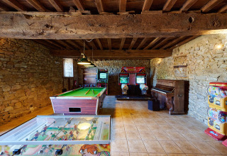 Sala giochi con muri in pietra, biliardo, calcetto, giochi arcade e pianoforte al Camping Domaine du Logis.