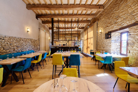 Zona de restaurante con sillas coloridas y paredes de piedra en Camping Domaine du Logis, Bretaña, Francia.