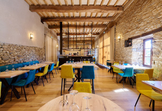 Restaurantområde med farverige stole og stenvæg i Camping Domaine du Logis, Bretagne, Frankrig.