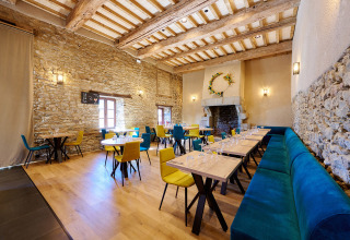Licht restaurantinterieur met stenen muren, houten balken en kleurrijke stoelen bij Camping Domaine du Logis, Bretagne.