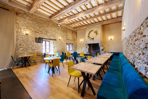 Licht restaurantinterieur met stenen muren, houten balken en kleurrijke stoelen bij Camping Domaine du Logis, Bretagne.