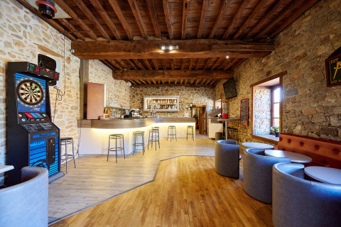 Acogedor bar con paredes de piedra, máquina de dardos y asientos en Camping Domaine du Logis en Bretaña.