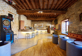Accogliente bar con muri in pietra, freccette e area lounge al Camping Domaine du Logis in Bretagna, Francia.