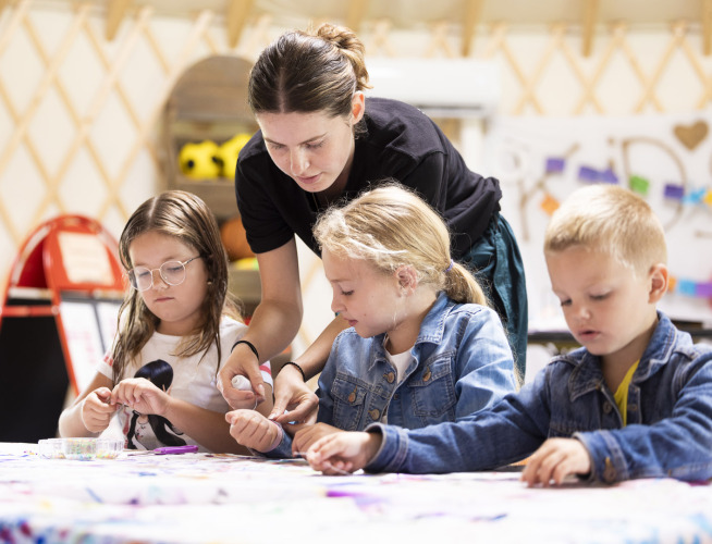 Lehrerin unterstützt Kinder beim Basteln am Tisch im Camping Domaine du Logis in der Bretagne, Frankreich.