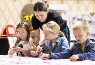 Insegnante aiuta i bambini con lavoretti manuali al tavolo al Camping Domaine du Logis in Bretagna, Francia.
