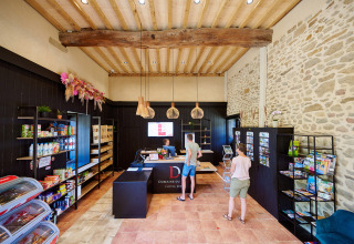 Interiør af receptionen og butikken på Camping Domaine du Logis, med besøgende og informationsbrochurer.