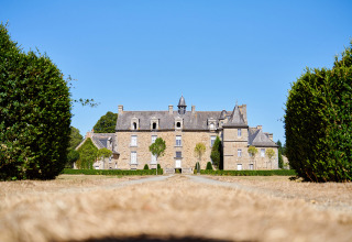 Allée bordée de haies menant à un château au Camping Domaine du Logis, un parc de vacances en Bretagne, France.