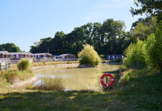 Feriepark med hytter ved en lille sø på Camping Domaine du Logis i Bretagne, Frankrig, omgivet af natur.