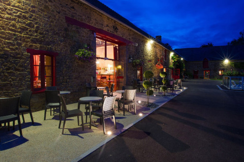 Terraza exterior con mesas y sillas en Camping Domaine du Logis, Bretaña, Francia, al atardecer.