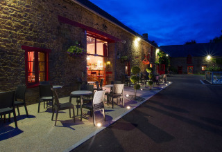 Udendørs terrasse med borde og stole på Camping Domaine du Logis i Bretagne, Frankrig, aftenstemning.