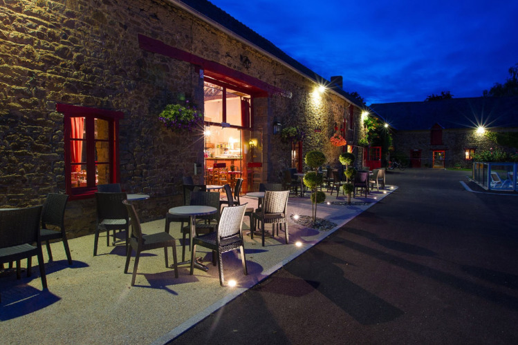 Beleuchtete Außenterrasse mit Sitzplätzen im Camping Domaine du Logis, Bretagne, Frankreich, abends.