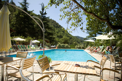 Piscina con tumbonas y mesas en el parque de vacaciones Camping Delle Rose en Liguria, Italia, rodeada de colinas.