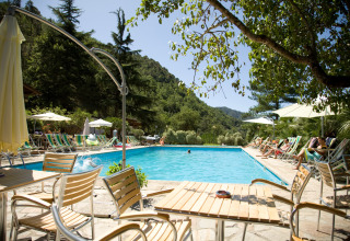 Zwembad met ligstoelen en tafels in Camping Delle Rose, een vakantiepark in Ligurië, Italië, tussen de heuvels.